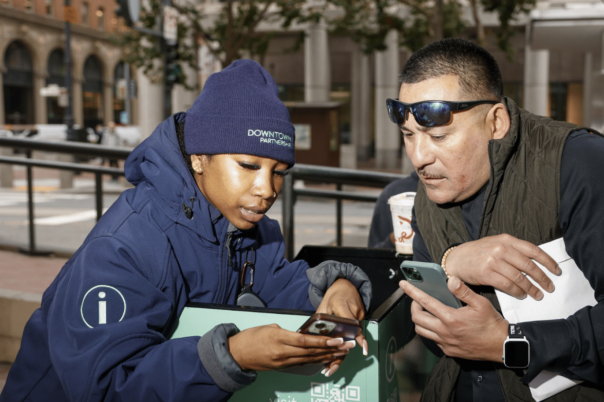 Ambassador assisting a man with a smartphone at a Market Street BART stop
