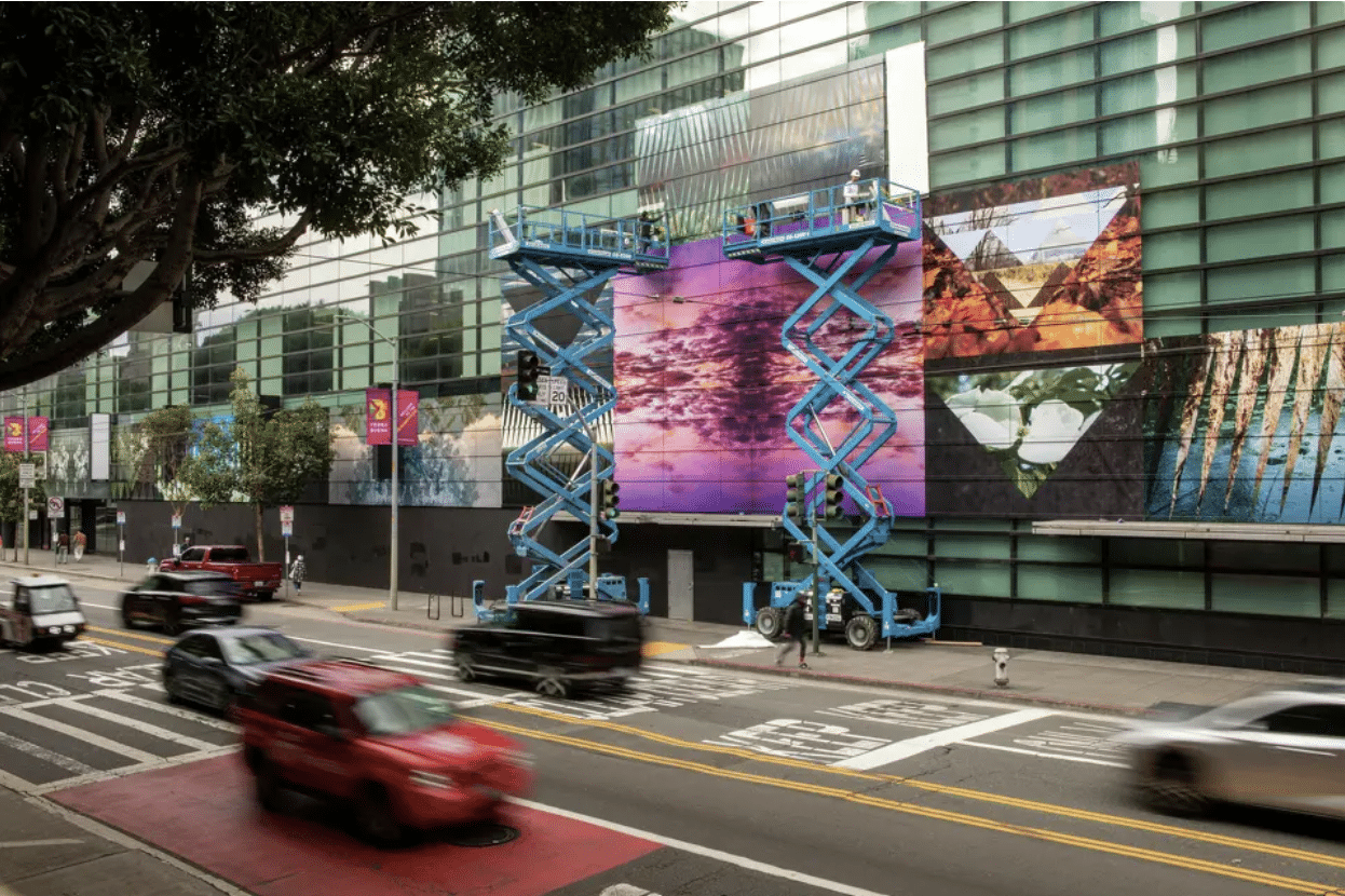 Workers installing large colorful art panels on the exterior of a downtown San Francisco building