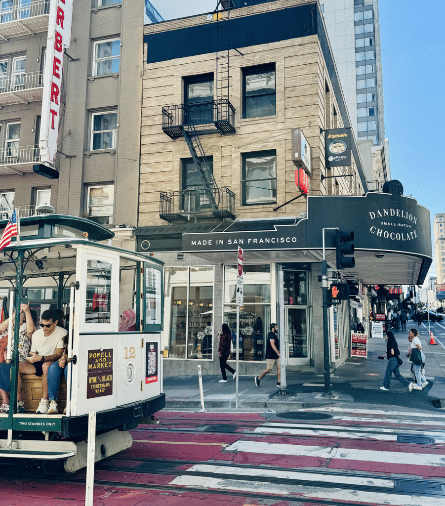 San Francisco cable car passing Dandelion Chocolate storefront on a downtown street corner
