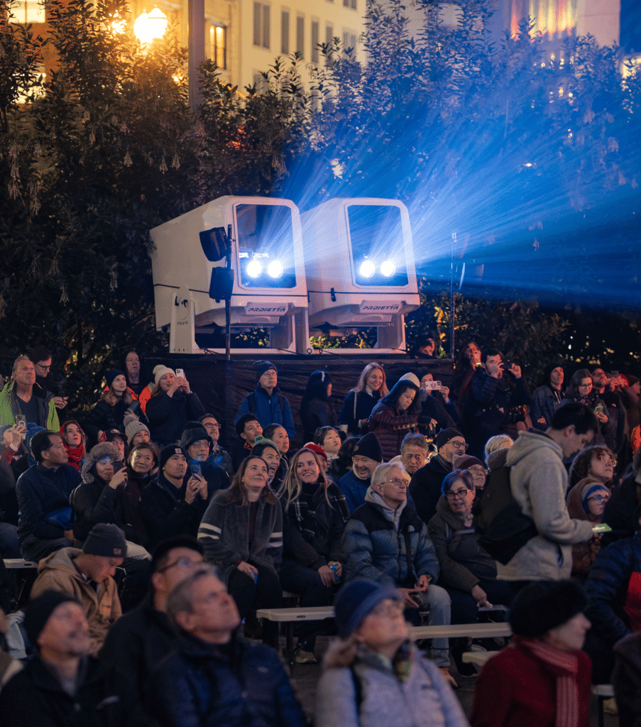 Crowd gathered outdoors at night watching a public projection or light show
