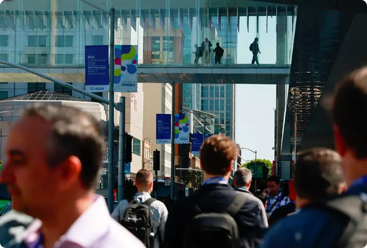 People walking along a downtown San Francisco street beneath a glass pedestrian skybridge