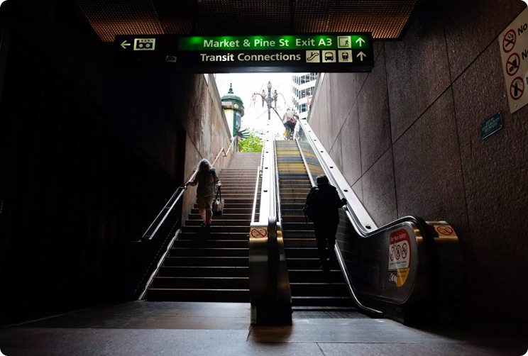 People walking up stairs and escalator inside a downtown San Francisco BART station