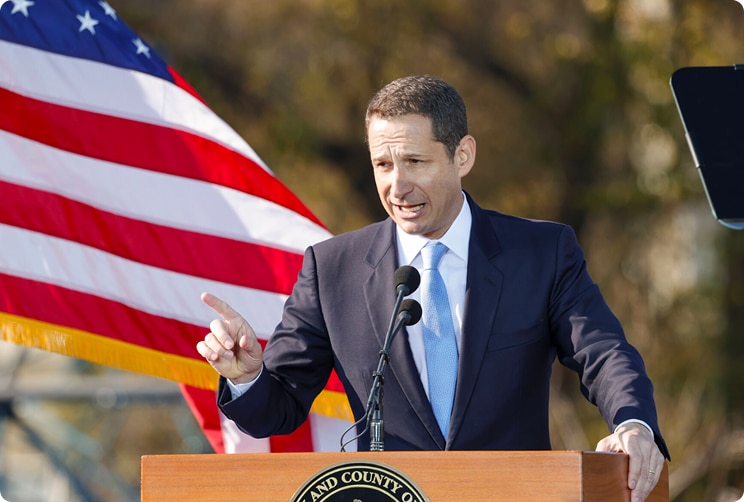 San Francisco Mayor Daniel Lurie speaking at a podium with an American flag in the background