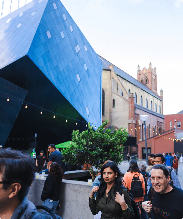 People walking along Yerba Buena Lane beside a modern blue building in downtown San Francisco