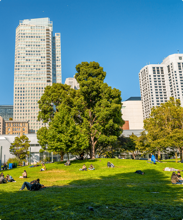 People relaxing on a grassy lawn in Yerba Buena Gardens with downtown San Francisco buildings in the background